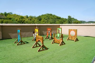 Bulk preschool obstacle course equipment featuring a multi-piece kindergarten outdoor play wooden crawl-through gates set with colorful geometric cutouts on synthetic grass.