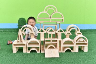 Child beside a large castle built with 58-piece hollow rubberwood building blocks, arches and rectangular beams