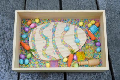 Easter sensory bin with colorful rice Easter eggs carrots wooden scoop and wooden sensory tray