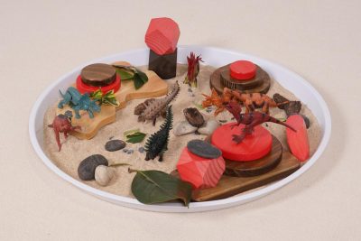 dinosaur small world play set with sand, wooden desert scenery and dinosaur figures in a circular play tray