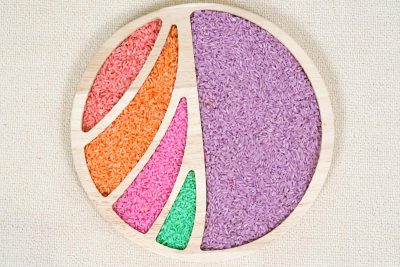 round wooden sensory tray with divided sections filled with colorful rice